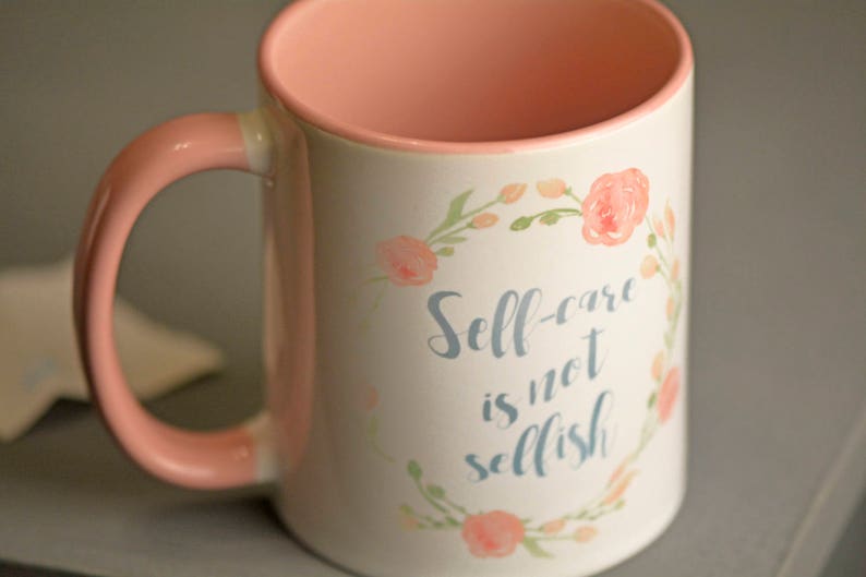 May include: A pink and white ceramic mug with a floral design and the text "Self-care is not selfish".