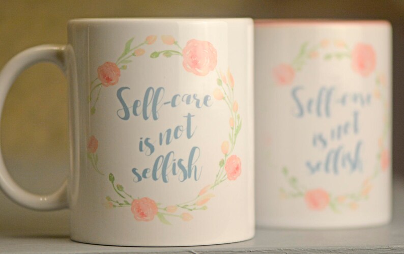 May include: Two white ceramic mugs with a floral design and the text "Self-care is not selfish" in blue lettering.