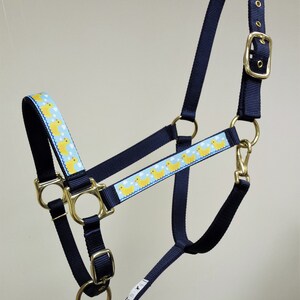 May include: A navy blue horse halter with a yellow rubber ducky pattern on the noseband. The halter has gold-colored hardware.