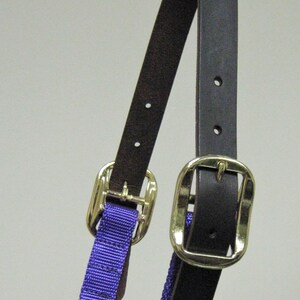Puede incluir: Un cabezal de caballo de nylon morado con una cabezada de cuero marr&oacute;n y dos hebillas doradas.