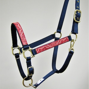 Puede incluir: Un cabezal para caballo azul marino con estampado de bandana rojo. El cabezal tiene una hebilla de lat&oacute;n y dos anillos de lat&oacute;n.