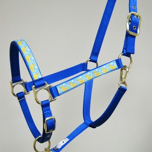 May include: Blue nylon horse halter with a yellow rubber ducky pattern. The halter has a brass buckle and two brass rings.