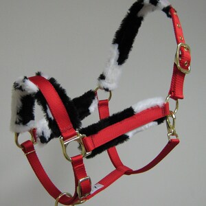 May include: Red horse halter with black and white faux fur trim. The halter has a brass buckle and rings.