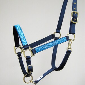 Puede incluir: Un cabezal de caballo azul y negro con un patr&oacute;n de paisley. El cabezal tiene herrajes dorados y una hebilla.
