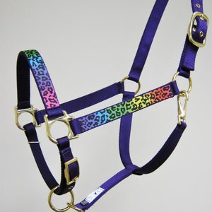 Pode incluir: Um cabresto roxo para cavalo com um design de leopardo arco-&iacute;ris e ferragens douradas.