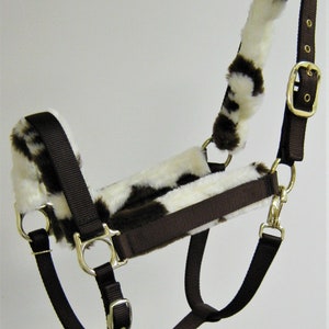 May include: Brown nylon horse halter with a white and brown faux fur lining. The halter has a buckle on the side and a metal ring on the nose.
