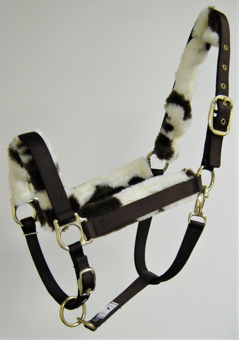 May include: Brown nylon horse halter with a white and brown faux fur lining. The halter has a buckle on the side and a metal ring on the nose.
