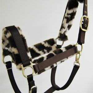 May include: Brown and white horse halter with fleece lining. The halter has a buckle on the side and a snap on the chin.