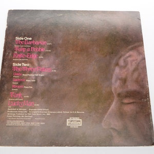 May include: Vintage vinyl record album cover with a brown and tan background. The album's tracklist is visible in pink text, including songs like "The Barbarian" and "Lucky Man." A side profile of a face is on the right side of the cover.