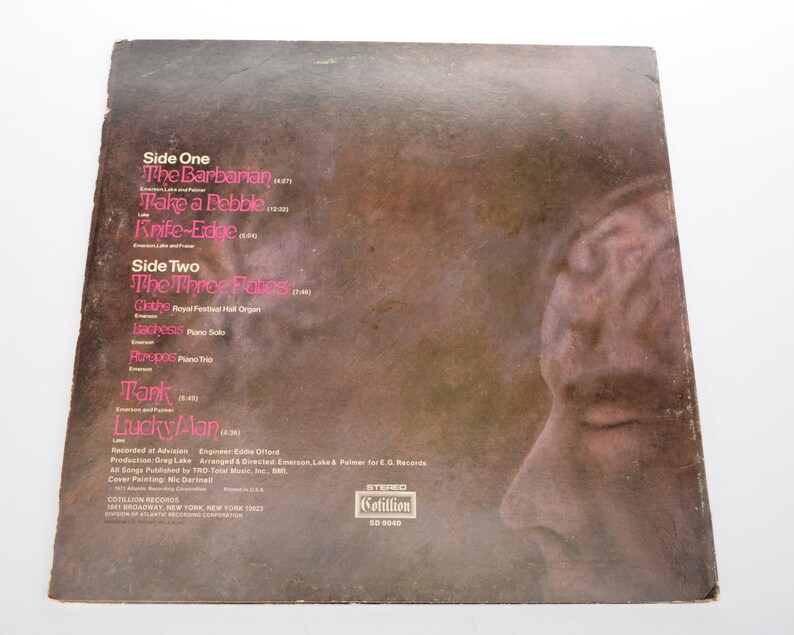 May include: Vintage vinyl record album cover with a brown and tan background. The album's tracklist is visible in pink text, including songs like "The Barbarian" and "Lucky Man." A side profile of a face is on the right side of the cover.