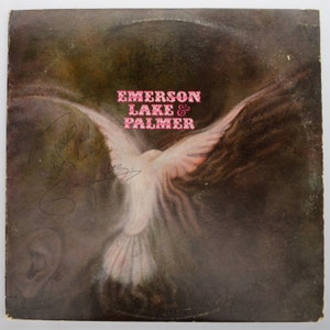 May include: Vintage vinyl record album cover for Emerson, Lake & Palmer, featuring a white dove with outstretched wings against a dark, textured background. The band's name is in pink text. Includes signatures.