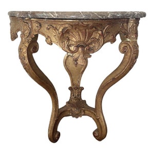 May include: A gold-painted, ornately carved wooden console table with a marble top. The table has a curved, heart-shaped base with intricate details.
