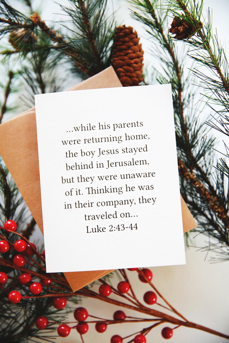 May include: A white card with a Christmas-themed quote from the Bible, Luke 2:43-44, about Jesus staying behind in Jerusalem. The card is surrounded by green pine branches and red berries.