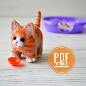 May include: A felted orange and white cat with black eyes and a pink nose. The cat is standing on a wooden surface with a small orange bowl in front of it. The text "PDF TUTORIAL" is on a circle in the lower right corner of the image.