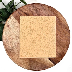 May include: A square sheet of beige parchment paper with a speckled texture. The paper has the text "The Sea Salt Co" and "Stucco" printed on it.