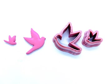 May include: Four pink plastic cookie cutters shaped like birds. The cutters are in different sizes, with the largest cutter in the centre of the image.