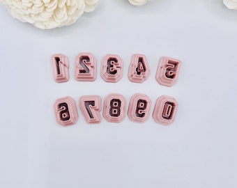 May include: A set of ten pink plastic number cookie cutters, numbered 0 through 9. The cutters are arranged in two rows, with the numbers 1 through 5 in the top row and 6 through 0 in the bottom row.