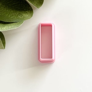 May include: A pink plastic cookie cutter shaped like a rectangle.