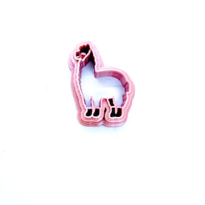 May include: A pink plastic cookie cutter shaped like a llama. The cutter has a detailed outline of the llama's body, head, and legs.