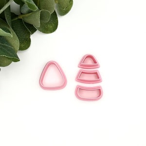 May include: A set of four pink plastic cookie cutters shaped like a triangle and a three-tiered cone.