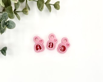 May include: Three pink plastic cookie cutters shaped like the numbers 1, 2, and 3. Each number has a small heart on top.