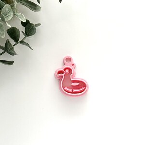 May include: Pink plastic charm shaped like a flamingo pool float. The charm has a small heart detail on the top.