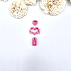 May include: A set of three pink plastic cookie cutters shaped like a flower. The cutters are arranged vertically, with the largest cutter at the top and the smallest cutter at the bottom.