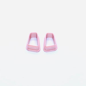 May include: Two pink plastic cookie cutters shaped like a rectangle with rounded corners.