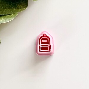 May include: Pink plastic cookie cutter shaped like a red backpack.