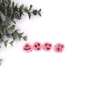 May include: Four pink plastic cookie cutters shaped like a Christmas tree, candy cane, stocking, and a present.
