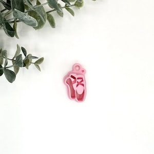 May include: Pink plastic ballerina shoe charm with a small heart detail.