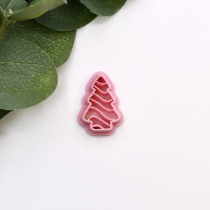May include: Pink plastic Christmas tree cookie cutter with a wavy design.
