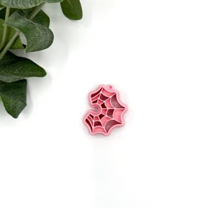 May include: A pink plastic spiderweb charm with a hole at the top for hanging.