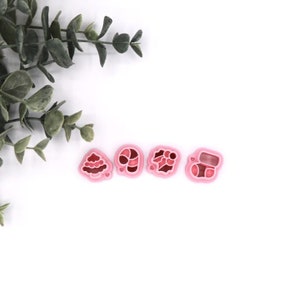May include: Four pink plastic cookie cutters shaped like a Christmas tree, candy cane, stocking, and a present.