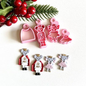 May include: A set of pink plastic cookie cutters shaped like a nutcracker, a ballerina, and a dress. There are also five fondant figures of a nutcracker, a ballerina, and three dresses.