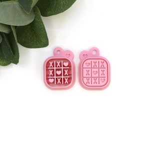 May include: Two pink plastic tic-tac-toe game pieces with hearts and X's.