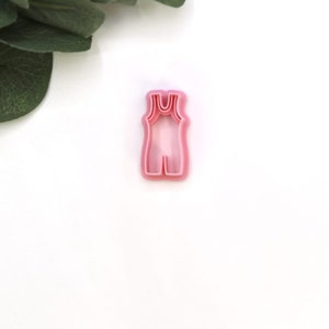 May include: Pink plastic cookie cutter shaped like a sleeveless leotard.