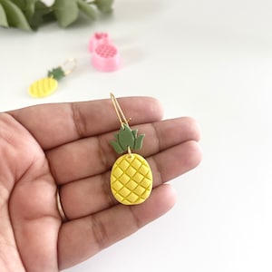 May include: Gold pineapple earrings with a yellow pineapple charm and a green leaf on top.