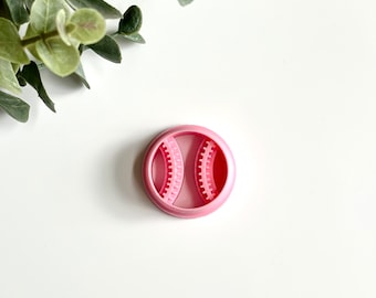 May include: Pink plastic cookie cutter shaped like a baseball. The cutter has a raised design of the baseball stitches.