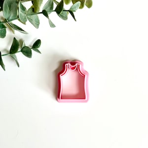 May include: Pink plastic cookie cutter shaped like a sleeveless shirt.