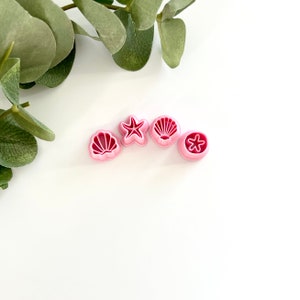 May include: Four pink plastic cookie cutters shaped like a seashell, a starfish, a seashell, and a starfish.