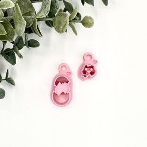 May include: Two pink plastic cookie cutters shaped like a baby's foot and a baby's foot with a heart on the toe.
