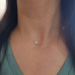 May include: A delicate, clear necklace with a small, white star charm featuring a blue evil eye design.