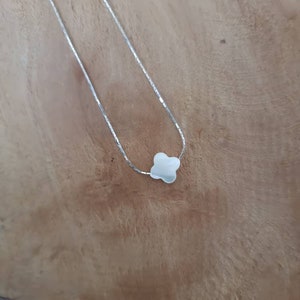 Könnte beinhalten: Eine silberne Kettenkette mit einem kleinen, weißen vierblättrigen Kleeblatt-Anhänger.