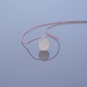 May include: A white, teardrop-shaped bead threaded on a thin pink cord.
