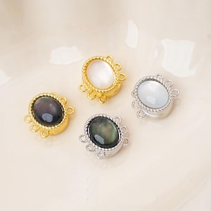 May include: Four oval jewelry connectors featuring smooth, polished cabochons in white and dark iridescent tones. Each piece is framed by a twisted metal border in gold or silver tones, with three small circular loops on each side for attachment.