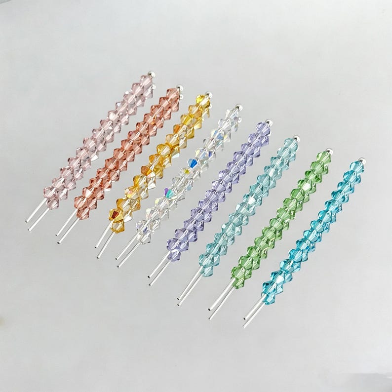 May include: An assortment of eight crystal hair pins in various colors, including pink, orange, yellow, clear, purple, teal, green, and blue. Each pin features a row of faceted crystals on a silver-colored wire.