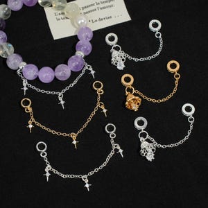 May include: A collection of jewelry charms and a beaded bracelet. The charms include gold and silver-toned chains with star and crystal accents, and small decorative pendants. The bracelet features purple and clear gemstone beads.