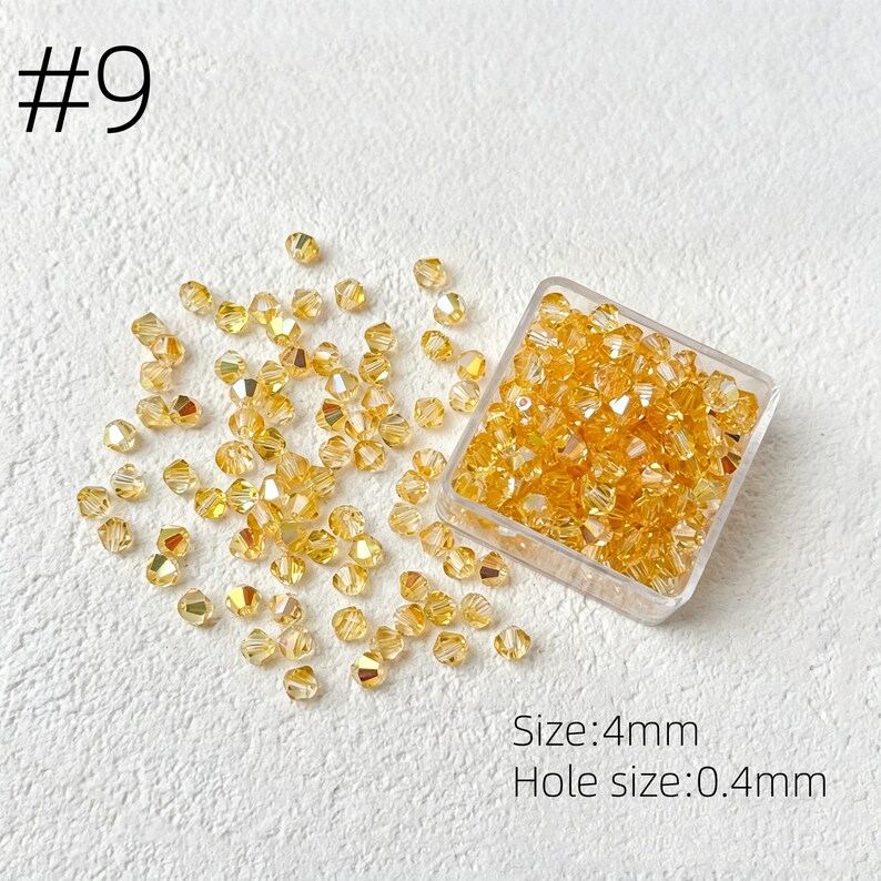 May include: A collection of golden-yellow, faceted beads, some scattered and some contained in a clear square container. The image includes the text "#9" and "Size: 4mm Hole size: 0.4mm".