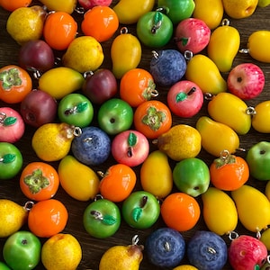 May include: A collection of colorful fruit-shaped charms, including apples, oranges, pears, and mangoes. The charms are in various shades of green, red, orange, yellow, and purple. Each charm has a small metal loop for attaching to jewelry or other crafts.